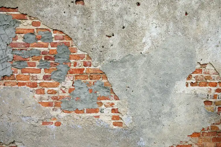 A weathered brick wall with patches of grey plaster and exposed red bricks, masonry repair