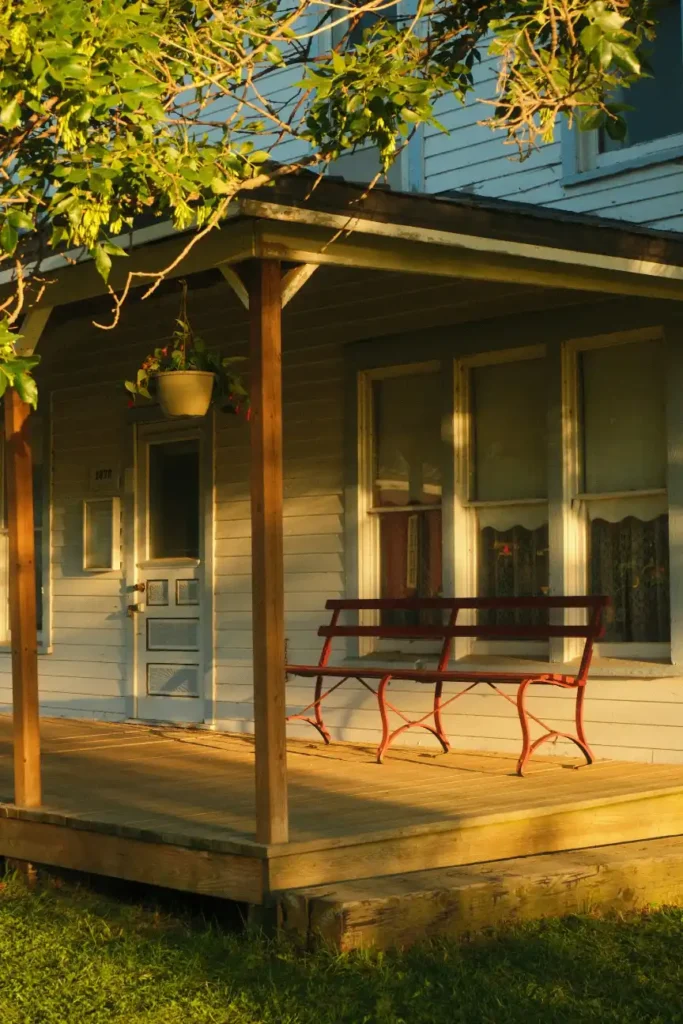 A red bench sits on a sunlit house porch, porch steps in Greenville NC