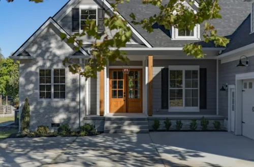 A suburban house with a stone facade, grey siding, and wooden double front doors, concrete driveway