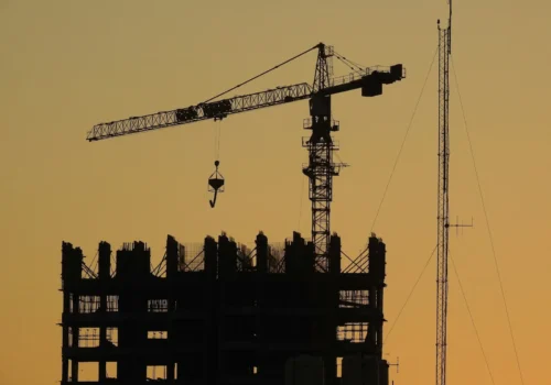 Construction crane and unfinished building silhouetted at sunset, concrete footing in Greenville NC