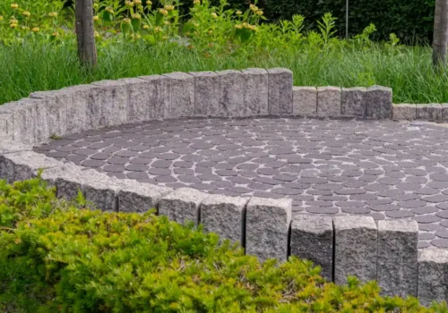 Round paver patio with a low stone seat wall in a backyard